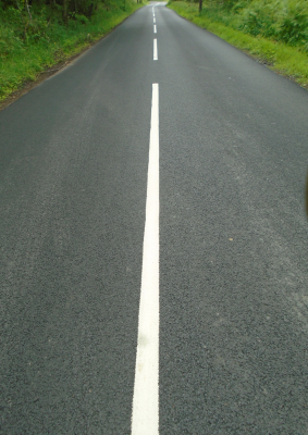 An image of smooth new tarmac, and bright white lines, contrasting with vivid green vegetation and leading the eye inexorably to the vanishing point in the composition.